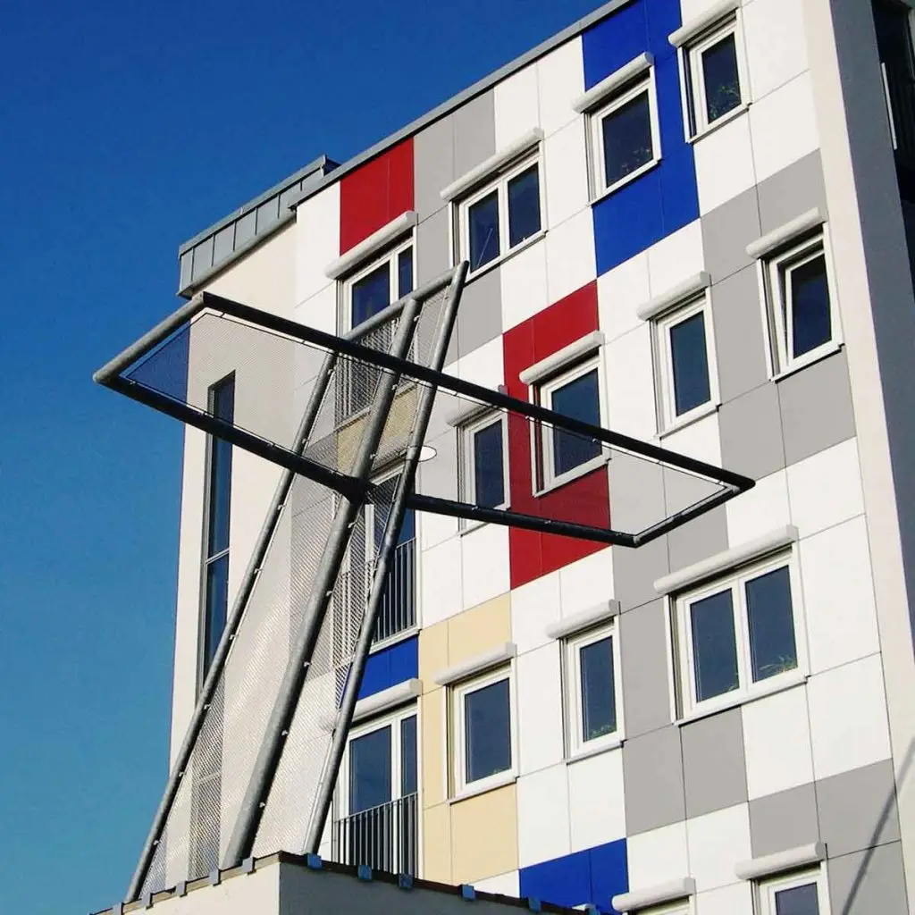 Eine Skulptur in Form eines Kreuzes vor einem bunten Haus