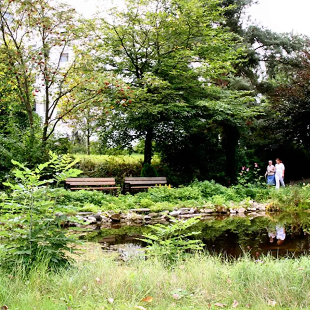 Ein parkähnlicher Garten, im Hintergrund gehen Menschen spazieren.