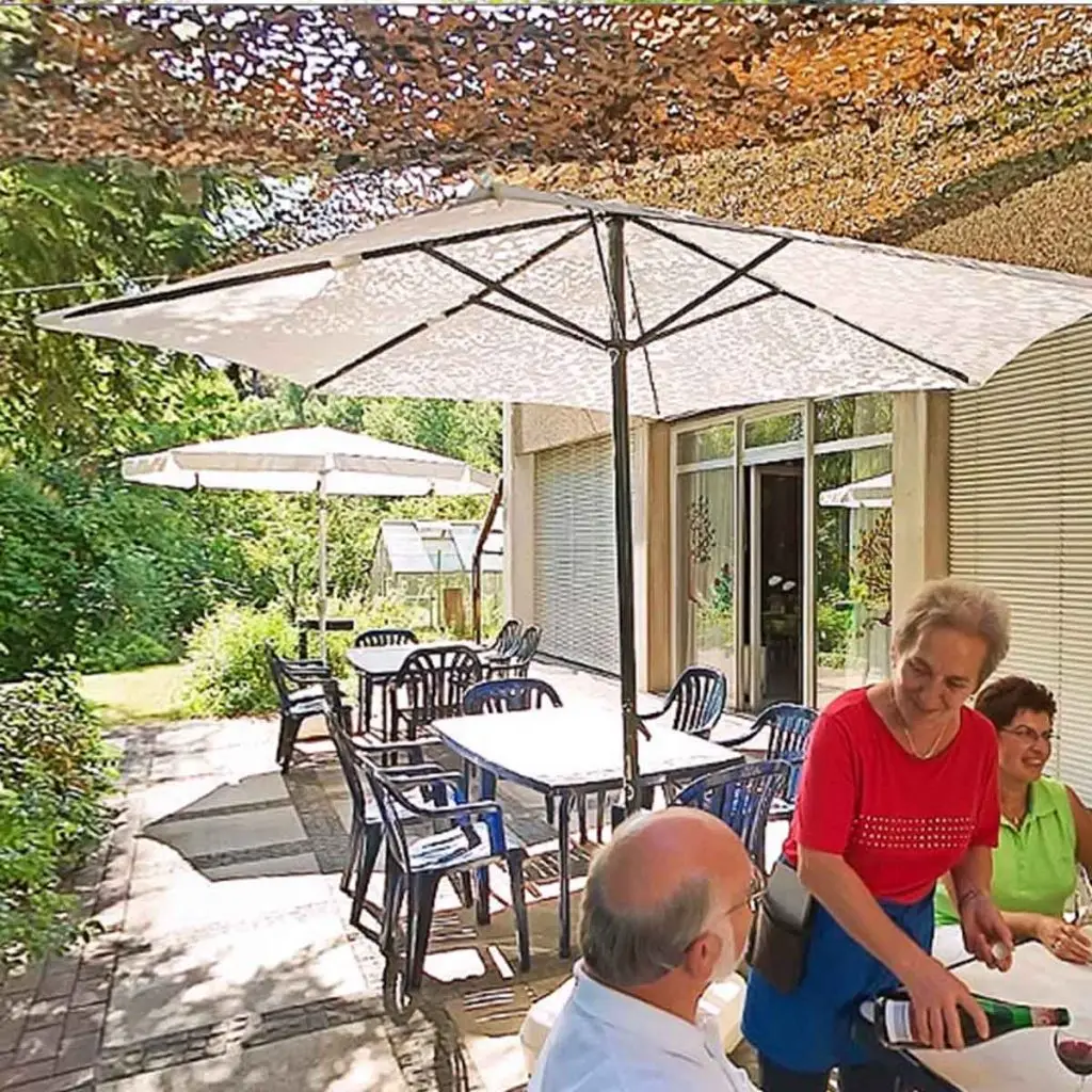 Eine Terrasse, im Vordergrund bedient eine Frau einen älteren Herren