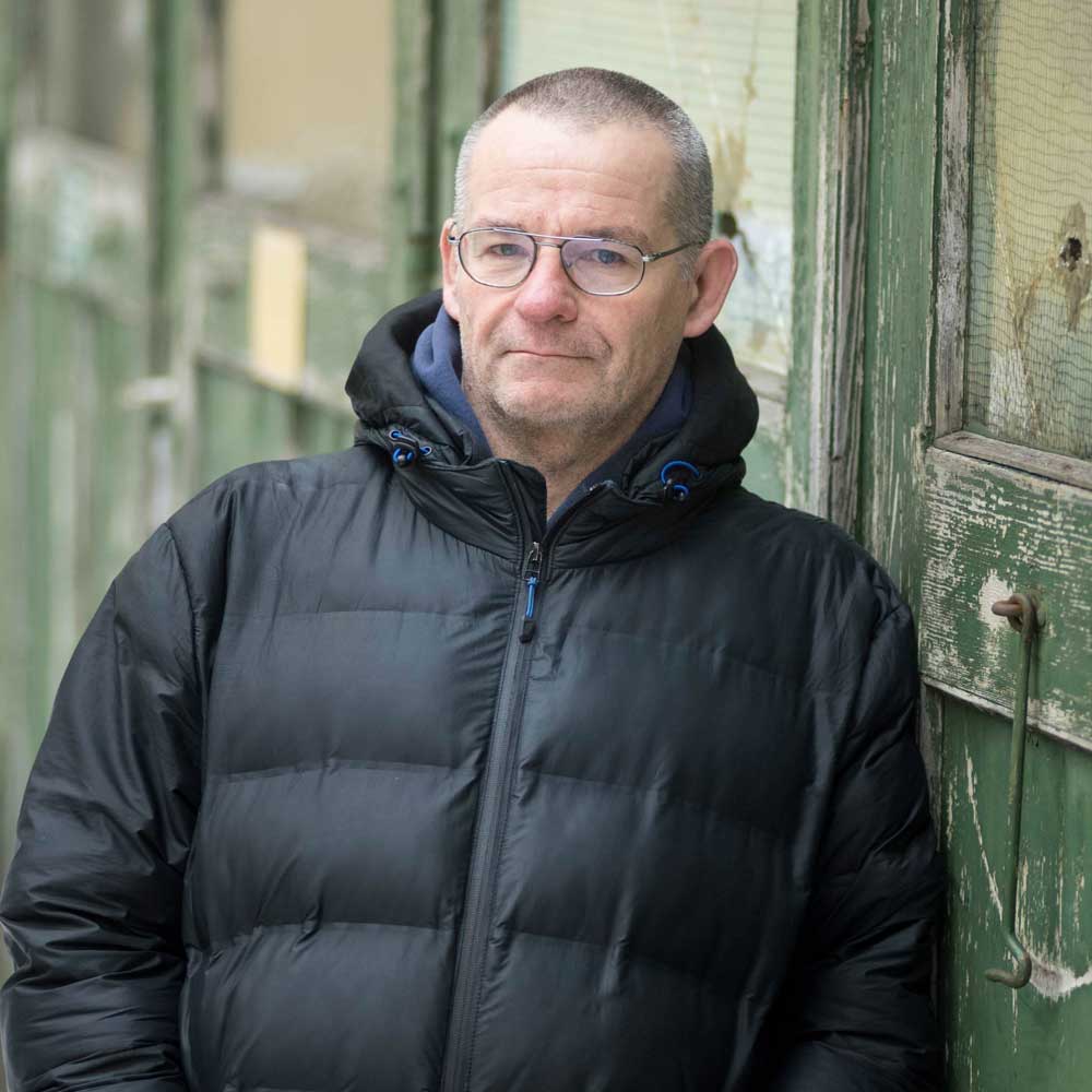 Ein Mann vor einer Haustür, er sieht in die Kamera