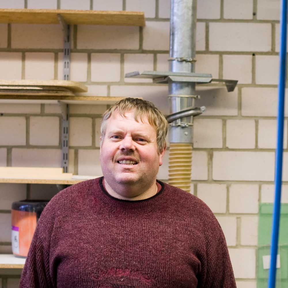 Ein Mann in einem roten Pullover vor einer Wand.