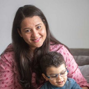 Eine Frau lächelt in die Kamera, sie hat einen kleinen Jungen auf dem Schoß.