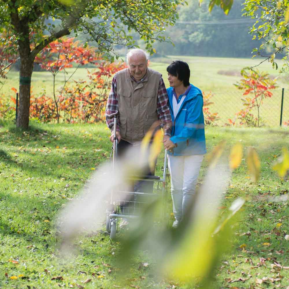 Eine Pflegerin begleitet einen Mann beim Spaziergang