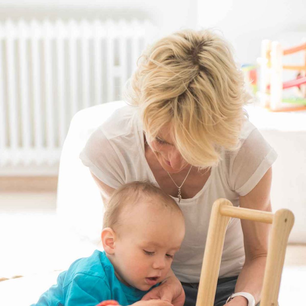 Eine blonde Frau beugt sich über ein spielendes Kind