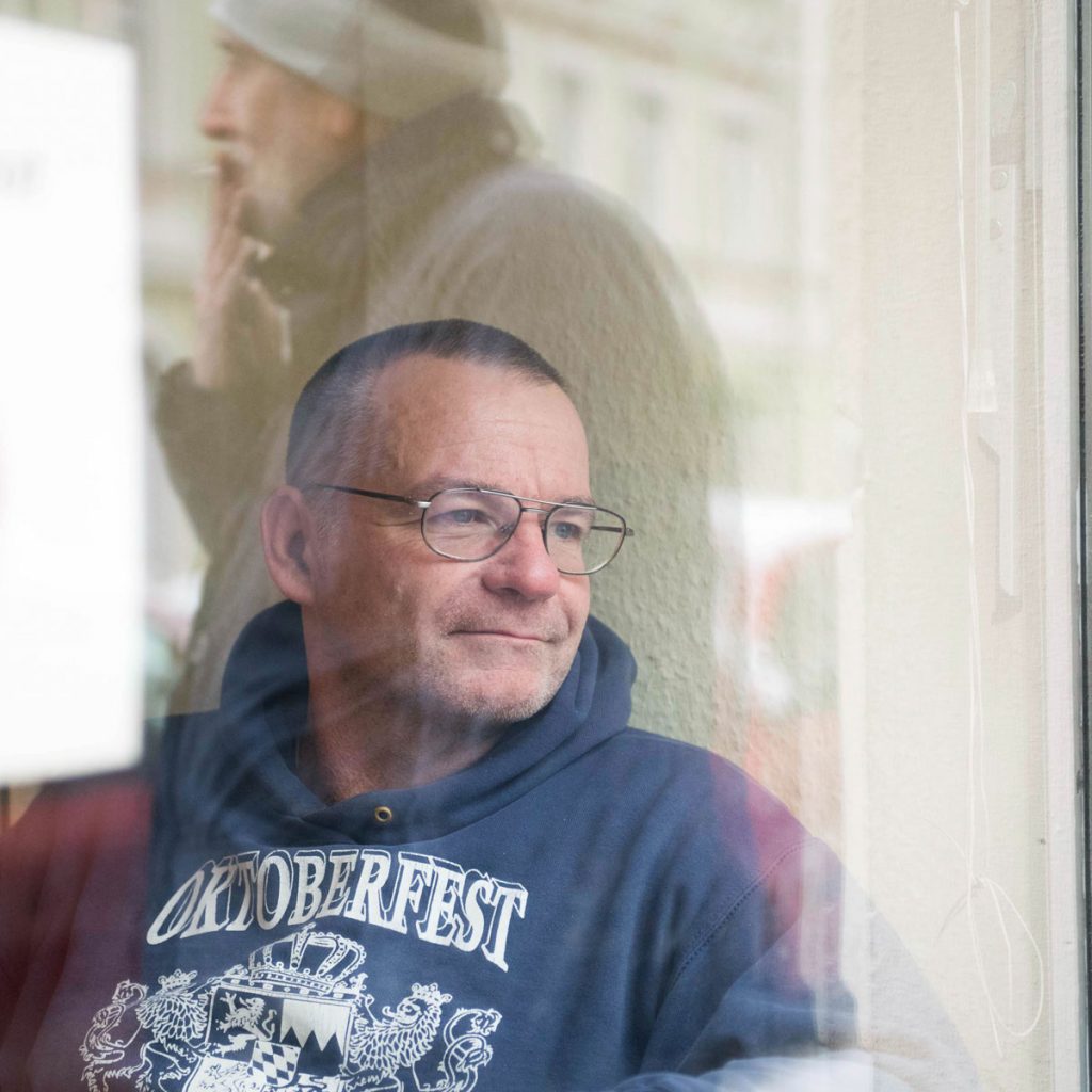 Ein Mann sieht aus dem Fenster. Im Glas spiegelt sich ein anderer Mann.